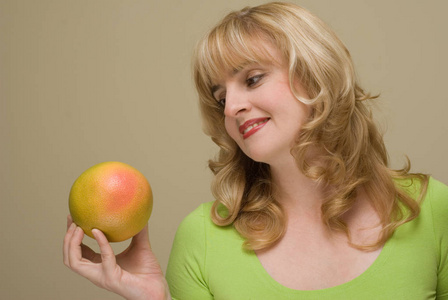 美丽的金发女郎微笑着拿着柚子摆在米色工作室背景