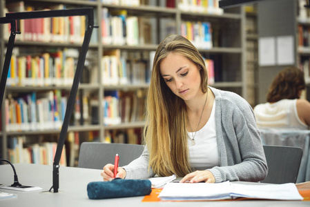 漂亮女学生笔记本电脑与学习在高中图书馆的咖啡