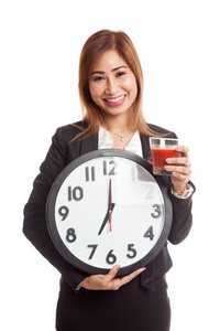 年轻的亚洲业务女人与番茄汁和时钟