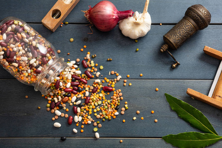 健康饮食观念。关闭玻璃罐中的豆类品种, 洒在木制桌面背景, 胡椒研磨机, 洋葱, 大蒜和磨碎机