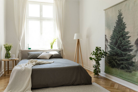 毯子在灰色床在白色卧室内部与窗口, 灯和花在桌上.真实照片照片