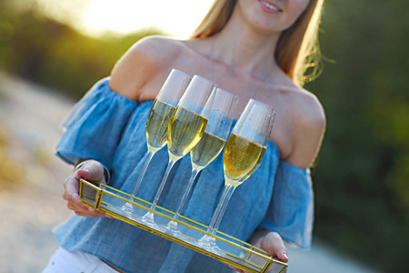 快乐的女人拿着香槟泡在沙滩上的玻璃杯。日落海滩派对