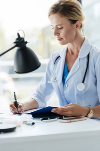自信的成年女医生白大衣与听诊器写在剪贴板在办公室表