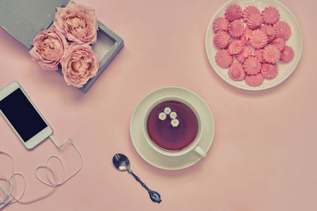 工作空间与智能手机, 一杯热草药茶, 鲜花和棉花糖在粉红色的桌子上。妇女工作桌为创造性。粉红色的项目仍然生活与柔和的口音。顶部视