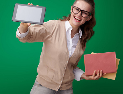 愉快的年轻学生妇女与书显示平板电脑空白屏幕反对绿色背景