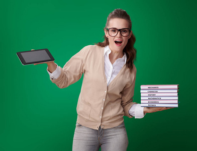 震惊的年轻学生妇女与书和平板电脑显示绿色背景下的技术便利性