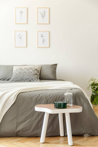 白色木桌在灰色床前面在极小的卧室内部与海报在模糊的背景。真实照片