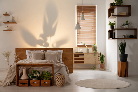 墙上的阴影, 在一个现代卧室内的床上, 木制货架, 盒子和植物。真实照片