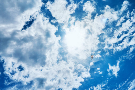 一只大在云层中漂浮在蓝天和明亮的夏日阳光下, 它由两条白绳子控制着, 飞向地面。