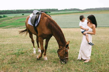 母亲抱着儿子看着马在田野上