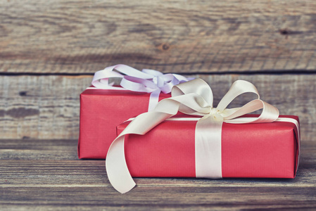 红色礼品盒裹着白色丝带和弓在老式的木墙背景与复制空间。礼物为圣诞节, 情人节, 生日或母亲节问候。节日包装概念