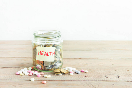玻璃罐子里有健康标签和药片的硬币。省钱, 健康预算和保险概念, 复制空间