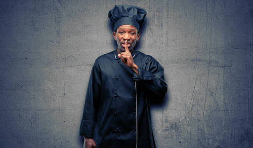 年轻的黑人厨师戴着食指在嘴唇上的主厨帽子, 要求安静。沉默和秘密概念