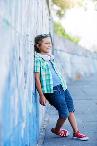 可爱的男孩用滑板在户外，站在大街上与不同的七彩涂鸦墙上