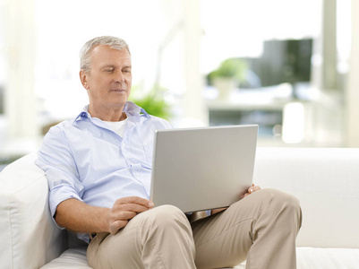 拍摄的一个老人在家中休息时使用他的笔记本电脑