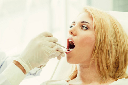 年轻英俊的牙医检查在牙科诊所坐在牙医椅上的快乐妇女病人的牙齿。牙科护理概念