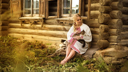 俄罗斯女人和一只猫在一个村子里的老木房子附近