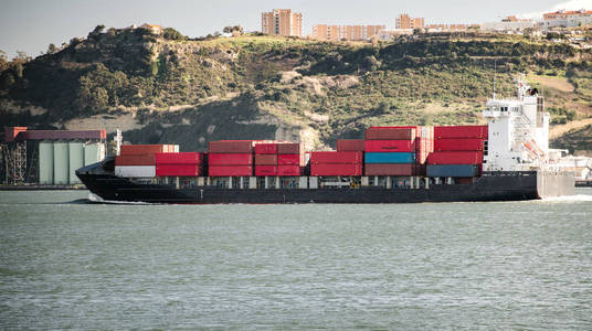 在阳光下的城市港湾波浪水中装载货船的侧面视图里斯本葡萄牙照片