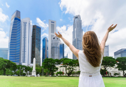 举起双手在草坪上摩天大楼背景的年轻女子