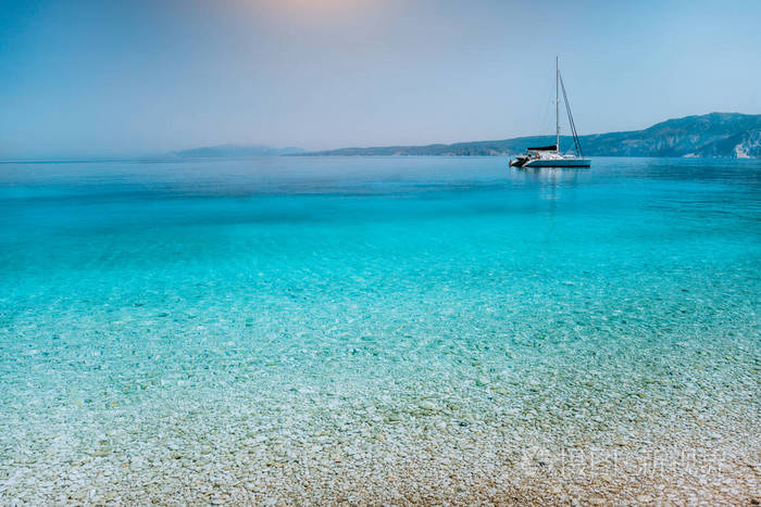 帆船双体游艇锚定在卵石滩附近与平静纯净湛蓝的水面