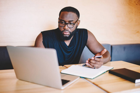 严重的非洲裔美国人千年男性看视频在笔记本电脑和手持智能手机, 集中深色皮肤人同步蜂窝多媒体与上网本使用应用