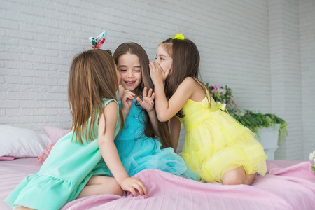 三个漂亮的小女孩坐在一张床上，互相耳语