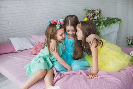 三个漂亮的小女孩坐在一张床上，彼此拥抱