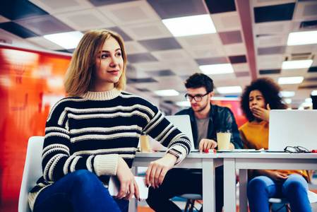 体贴的休闲穿着的学生坐在时髦的 coworking 空间, 手里拿着智能手机.