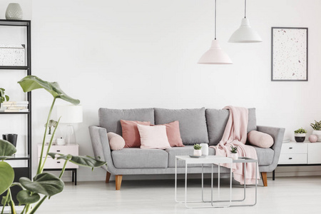 粉红色的垫子上灰色的沙发在白色客厅内部与灯具和海报。真实照片