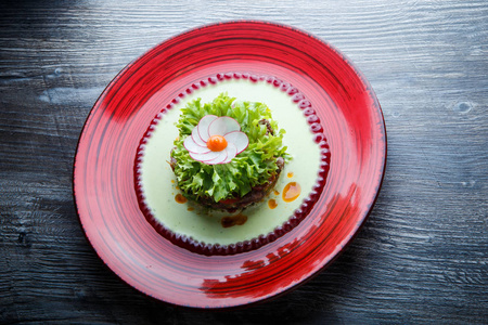 健康绿色沙拉配以萝卜在木桌上的红盘子上做的肉和花装饰