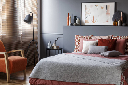 床上的灰色毯子在舒适的卧室内与橙色扶手椅和海报在床头板上