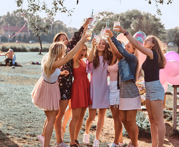 一群女朋友一起在户外公园庆祝生日的乐趣。快乐的朋友欢呼与果汁在野餐派对户外