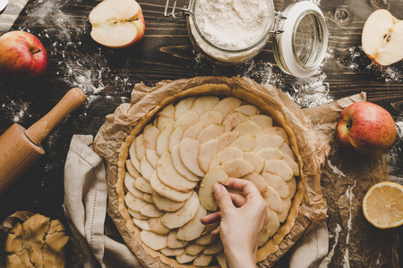 煮苹果派。把苹果切片添加到馅饼壳里。木桌上的苹果派配料
