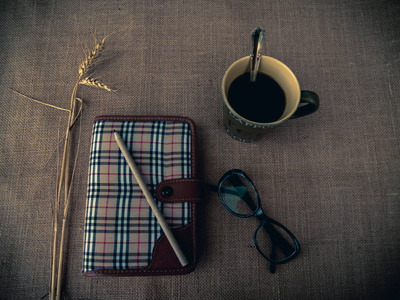 复古风格。有组织的办公桌与闭合的日志, 眼睛眼镜, 一杯咖啡, 干草, 铅笔和粗麻布背景