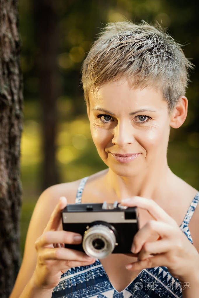 一个漂亮女人的肖像, 手里拿着照相机在夏天的森林里摆姿势.