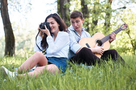 年轻夫妇在森林里漫步, 弹着吉他, 拍着老相机上的照片, 夏日的自然, 灿烂的阳光, 阴影和绿叶, 浪漫的情怀。