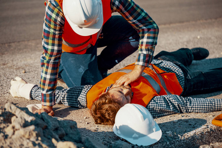 白盔工人在道路工程中检查受伤男子的生命功能