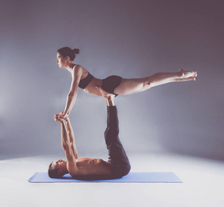 年轻夫妇一起练习杂技瑜伽工作室在垫子上。杂技。几个瑜伽。双人瑜伽
