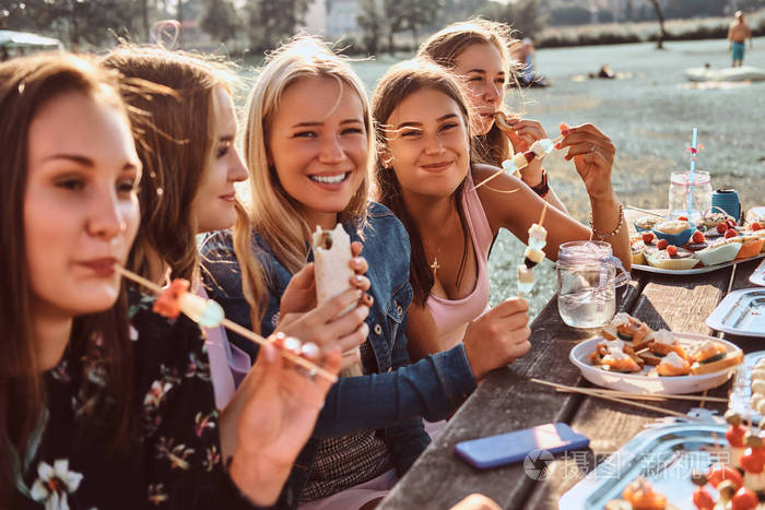 一群快乐的女朋友一起吃饭在餐桌上庆祝生日在户外公园