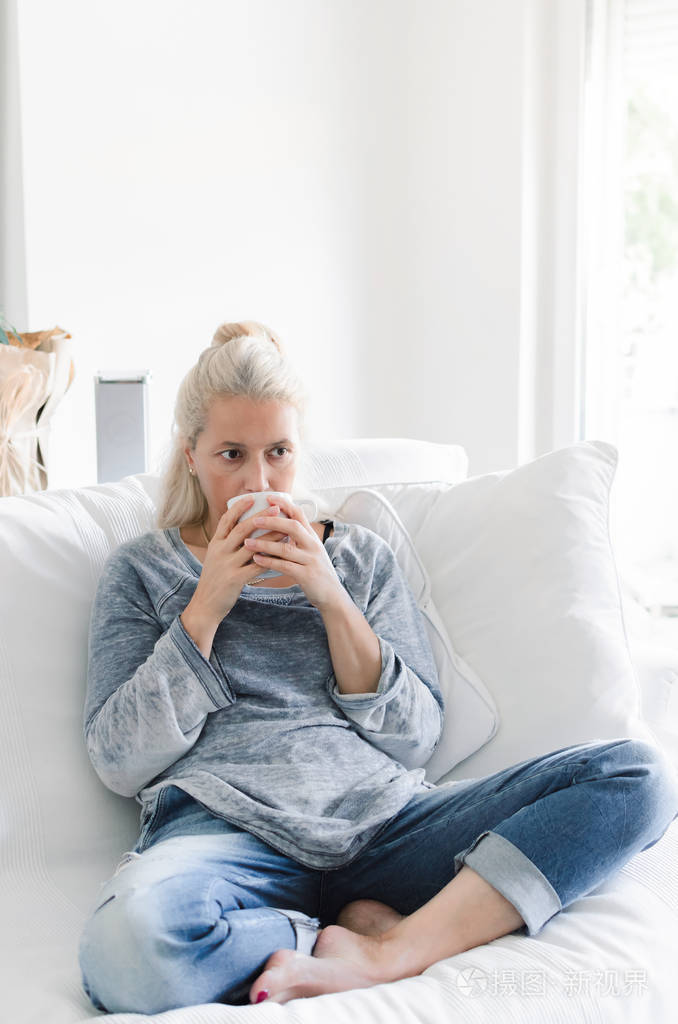 坐在沙发上的成年妇女在客厅与杯子在手