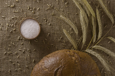 背景从粗麻布与黑麦面包, 耳朵的黑麦和盐瓶。顶部视图