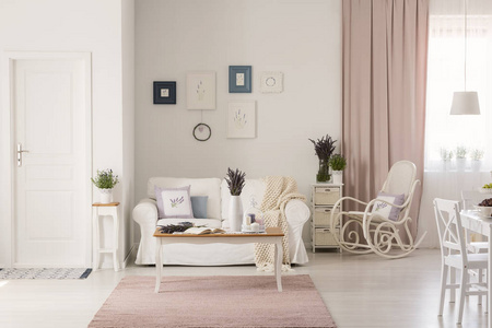 在白色客厅的粉红色地毯上的木桌, 沙发旁边有摇椅。真实照片
