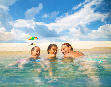 妈妈和女儿在浅水海里游泳.他们在美丽的海滩上欢笑和享受照片