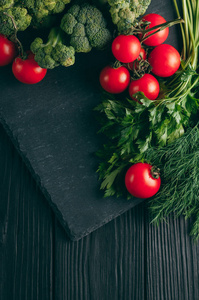 在一个黑色的木桌上, 新鲜的绿色花椰菜, 欧芹, 莳萝和樱桃西红柿为您的健康。食谱。成分。膳食食品。放置在文本之下。顶部视图