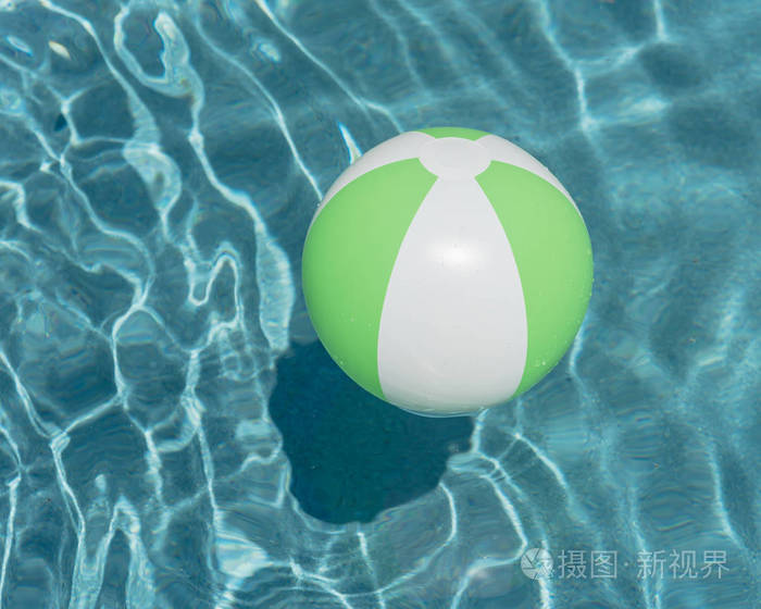 一个明亮的绿色海滩球在蓝色游泳池, 漂浮在清爽的游泳池与波浪反射在夏天太阳。活动假期背景。孩子的救命稻草。游泳池阳光明媚的一天