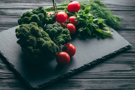 在一个黑色的木桌上, 新鲜的绿色花椰菜, 欧芹, 莳萝和樱桃西红柿为您的健康。食谱。成分。膳食食品。放置在文本之下。顶部视图