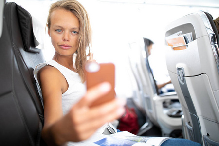 年轻快乐的妇女制作自拍照片与护照文件坐在飞机上的座位附近的窗口飞行期间在飞机上
