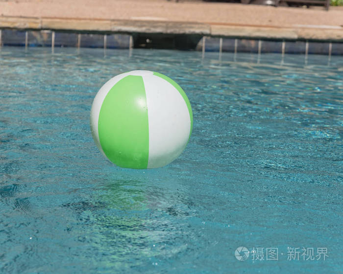 一个明亮的绿色沙滩球附近泳池应对边缘与深度标志。漂浮在清新的蓝色水中, 波浪反射在夏季太阳附近的泳池应对甲板和瓷砖。孩子的救命恩