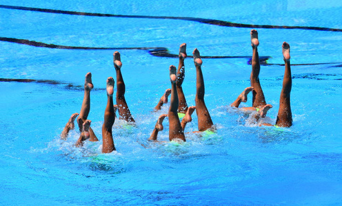 同步游泳者在行动中指出水的位置。同步游泳者腿部运动。同步游泳队执行在水中精心行动的同步例行