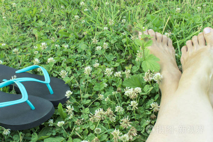 绿色草地上的两个蓝色和黑色的拖鞋和裁剪的女人腿